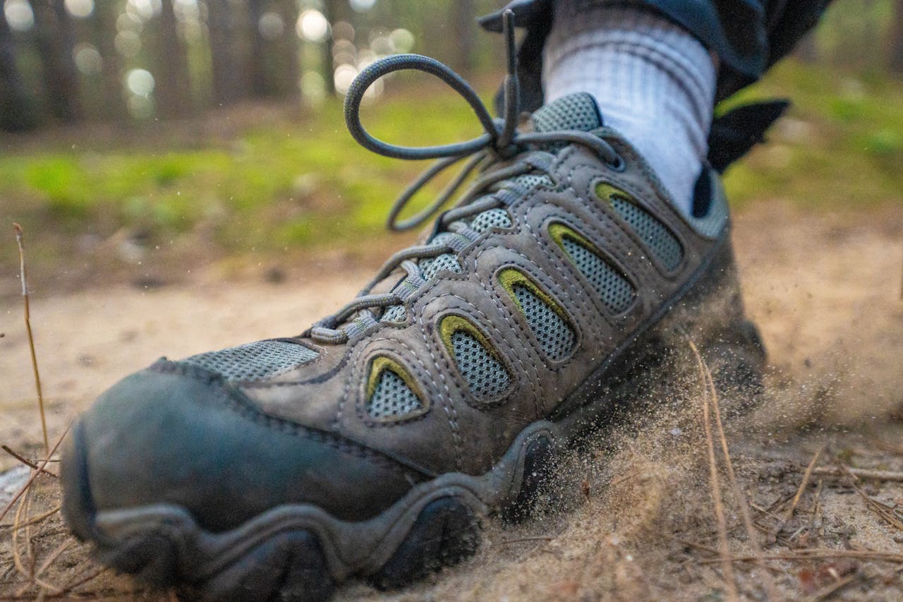 heros-img Close-up of a hiking boot kicking up sand on a forest trail, perfect for adventure themes.